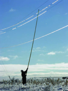 A lineworker breaks ice off power lines using a slip stick in a field of glass. 