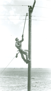 A lineman carefully reaches up to hang a fuse. From Dawson PPD’s archives.